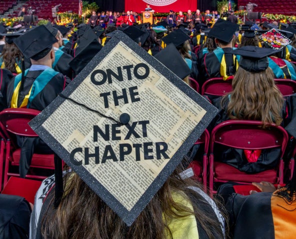 Photo showing a graduate from the back whose graduation cap reads "Onto the next chapter."